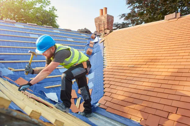 Construction worker in a blue hard hat and safety vest installing new shingles on a roof during a roof replacement project, ensuring the home's protection and longevity.