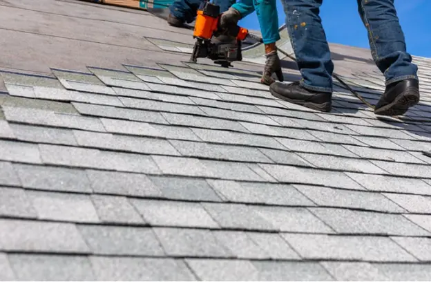 Roofing contractors installing new asphalt shingles on a residential roof, using nail guns for secure attachment and ensuring long-lasting protection.