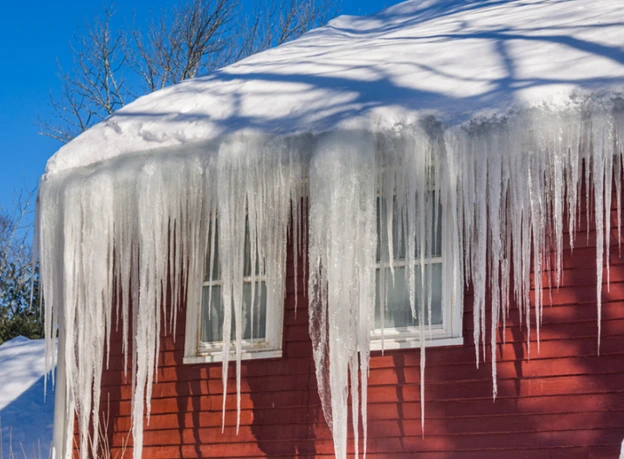 Ice dams and large icicles hanging from a snow-covered roof.