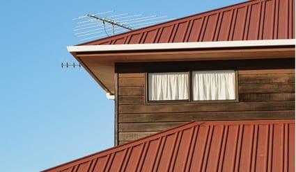 A close-up of a residential home with a red standing seam metal roof and dark wood siding, installed by Silverline Roofing Ltd