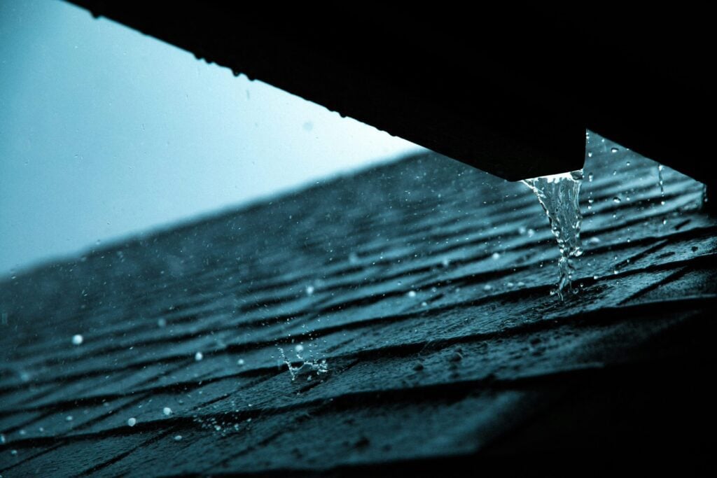 Rain falling on dark asphalt roof shingles with water streaming off the edge in Edmonton