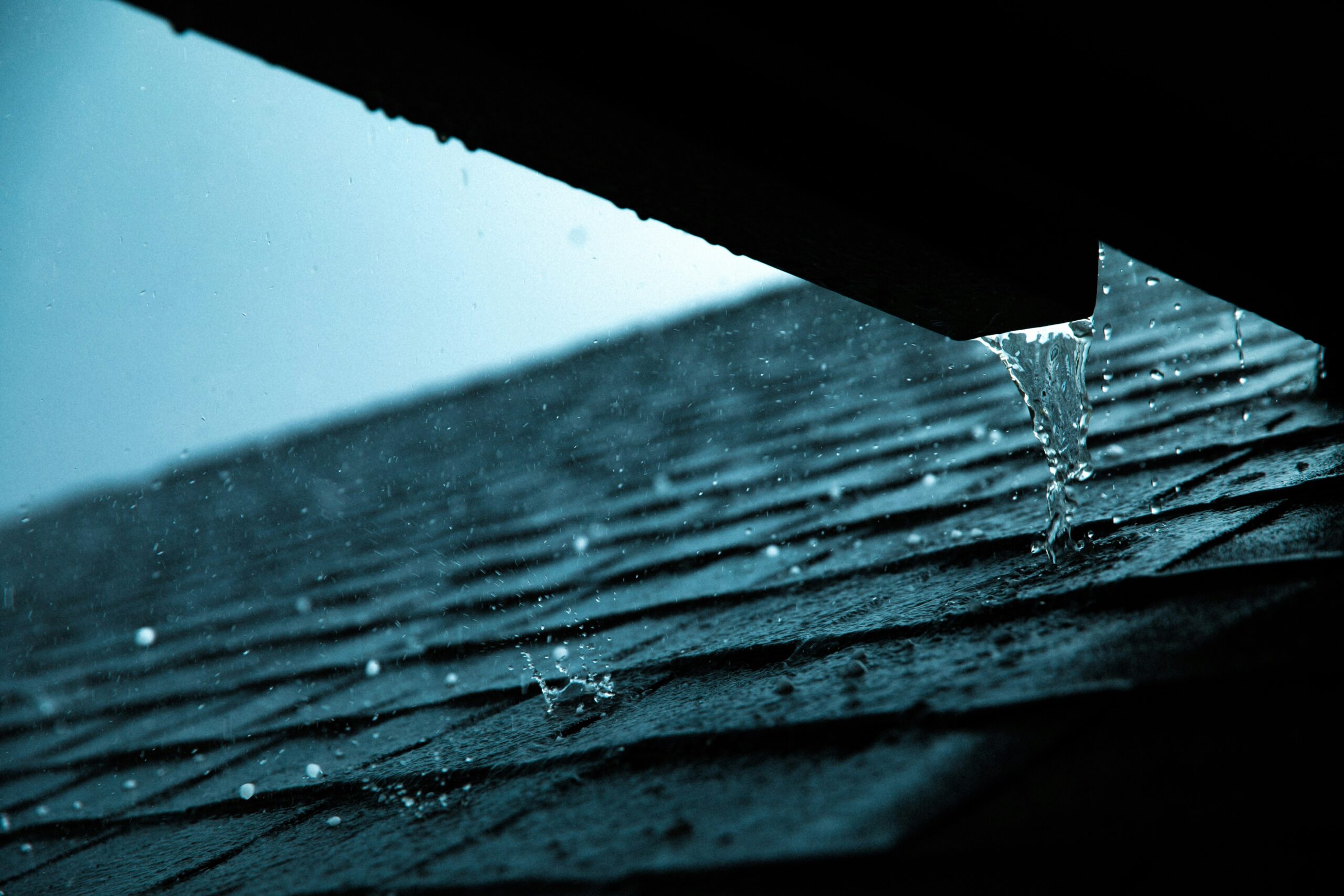 Rain falling on dark asphalt roof shingles with water streaming off the edge in Edmonton