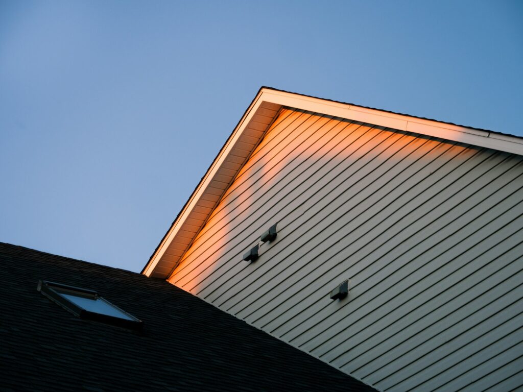 House gable showing where the roof, soffit and siding meet, lit by low sun