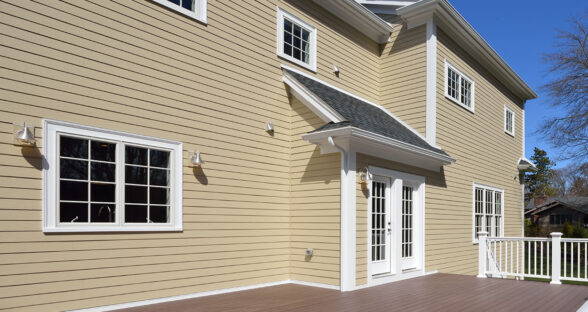 Composite deck in house backyard. Brown boards, white railing posts and veranda. Large, spacious, new construction.
